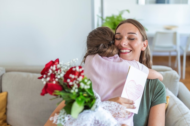 J'aime ma toi maman! Une jeune femme séduisante avec une petite fille mignonne passe du temps ensemble à la maison, remerciant pour la carte faite à la main avec le symbole de l'amour et les fleurs. Notion de famille heureuse. Fête des mères.