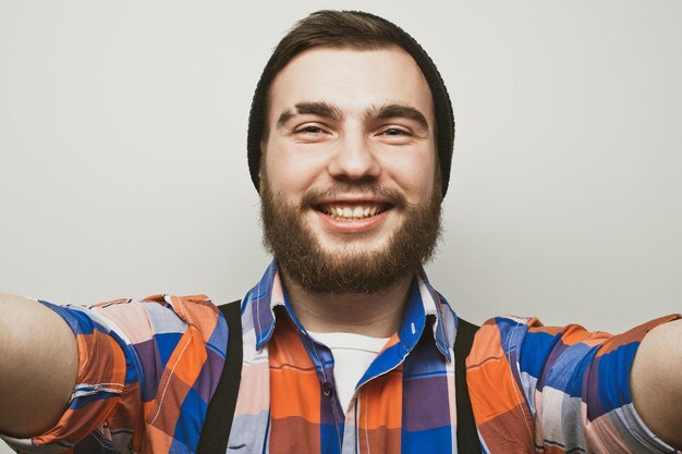 J'aime selfie Beau jeune homme barbu tenant un smartphone et faisant selfie et souriant en se tenant debout sur fond blanc