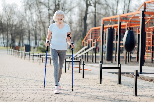 J'aime le sport. Femme blonde inspirée souriant et marchant à l'aide de béquilles