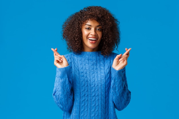 J'espère que mes voeux de nouvelle année se réaliseront. Enthousiaste, optimiste et optimiste belle femme afro-américaine en pull d'hiver, croisez les doigts pour la bonne chance et souriant excité, anticipez la réalisation du rêve