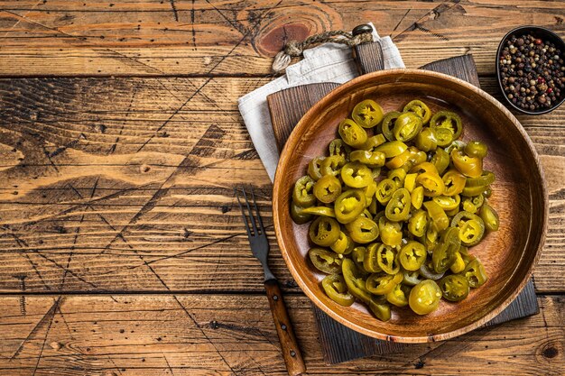 Jalapenos marinés et tranchés, dans une vieille assiette en bois. Fond en bois. Vue de dessus. Copiez l'espace.