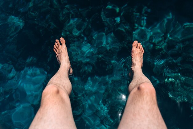 La jambe de l'homme suspendue à la jetée pieds nus avec le fond de la mer