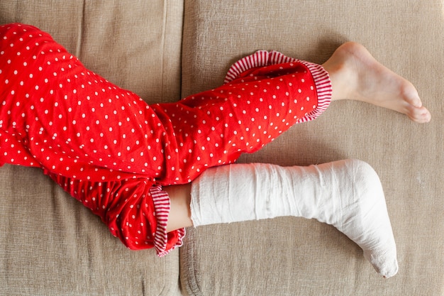 Jambe en plâtre d'une adolescente sur un canapé après une chute accidentelle avec une fracture de la cheville