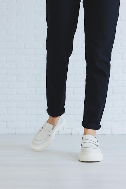 Jambes d'une belle jeune femme en pantalon noir et mocassins en cuir blanc élégants et modernes Nouvelle collection de chaussures pour femmes printemps été 2022