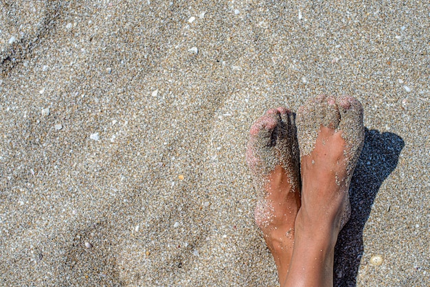 Jambes bronzées féminines sur la plage dans le sable.