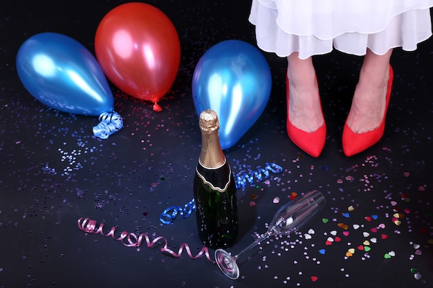 Photo jambes avec des confettis, du champagne et des ballons sur le sol