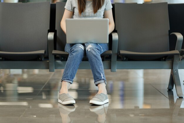 Jambes coupées d'une jeune femme touristique travaillant sur un ordinateur portable en attendant dans le hall de l'aéroport international