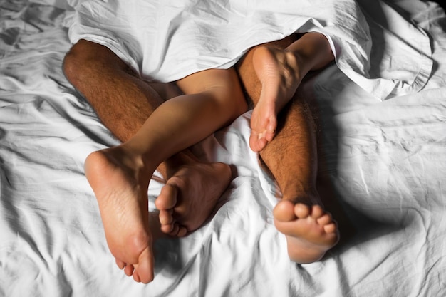 Jambes d'un couple d'amoureux se câlinant au lit sous les draps