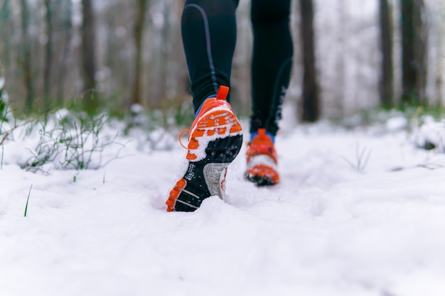 Jambes d'un coureur en baskets en faisant du jogging en hiver sur un chemin enneigé dans un parc