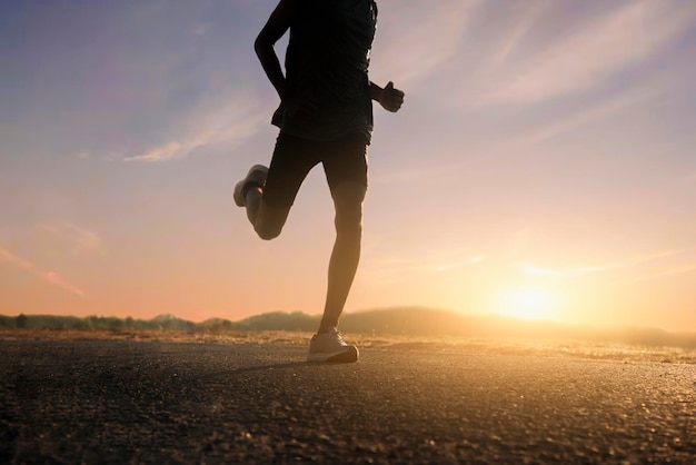 Photo jambes d'un coureur masculin courant sur la route au coucher du soleil.