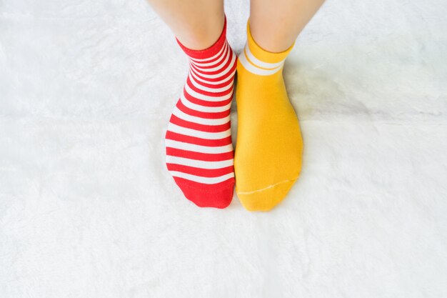 Jambes dans les chaussettes deux couleurs alternent, le côté rouge et jaune se tiennent sur le plancher de tissu blanc.