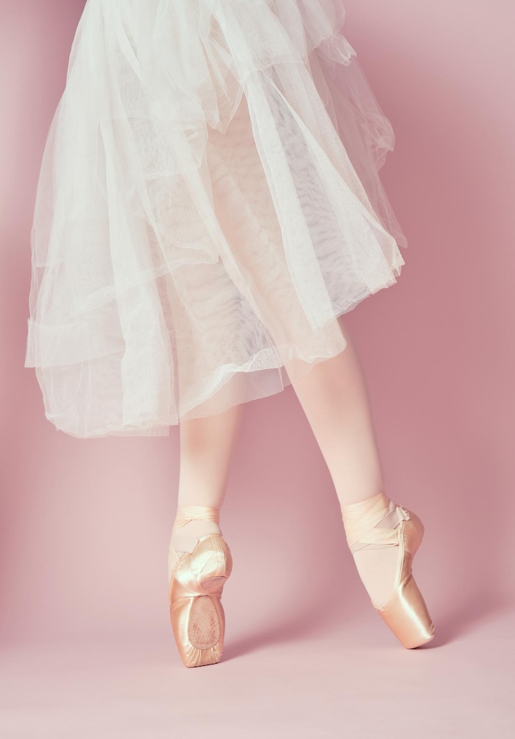 Photo jambes de danseuse de ballet classique portant des collants et une jupe blanche sur la pointe des pieds avec des chaussures de pointe de ballet sur fond rose
