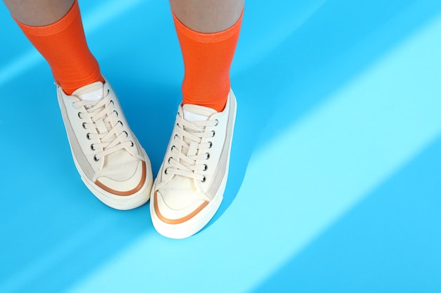 Jambes féminines en chaussettes oranges et baskets sur fond bleu