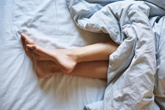 Jambes féminines dans le lit sous couverture