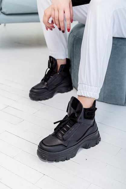 Jambes féminines élancées en pantalon blanc, baskets en cuir noir. Nouvelle collection de chaussures décontractées pour femmes