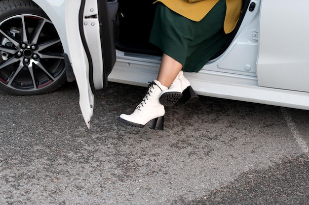 Jambes féminines élégantes en bottes blanches dans une nouvelle voiture sur le parking