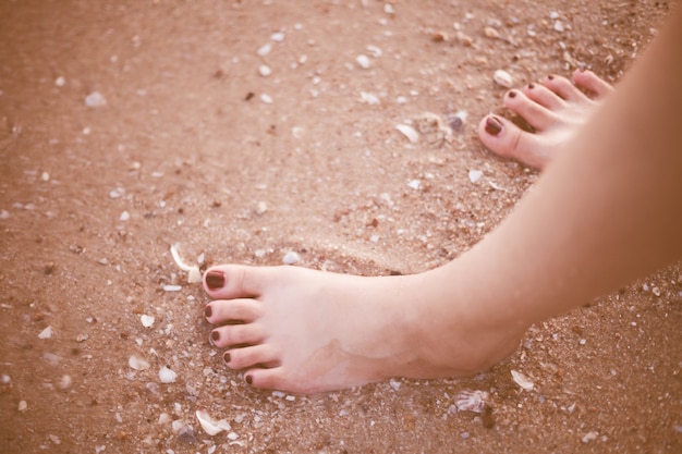 Jambes féminines pieds nus sur agrandi de plage de sable.