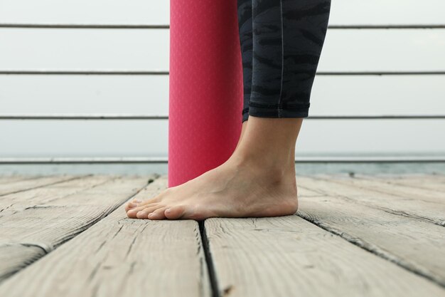 Photo des jambes féminines et un tapis de yoga rose sur le sol en bois en plein air