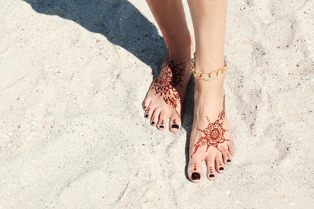 Jambes féminines avec tatouage au henné sur fond de sable de plage