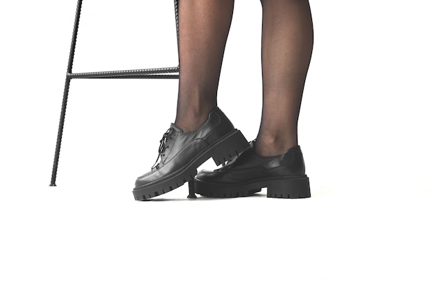 Jambes de femme en collants noirs et chaussures noires à côté d'une chaise isolée sur fond blanc
