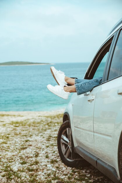 Les jambes de la femme dépassent de la voiture garée sur la plage de la mer. vacances d'été