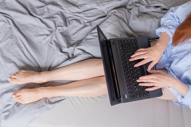 les jambes d'une femme inconnue dans le lit avec un ordinateur portable sur ses genoux