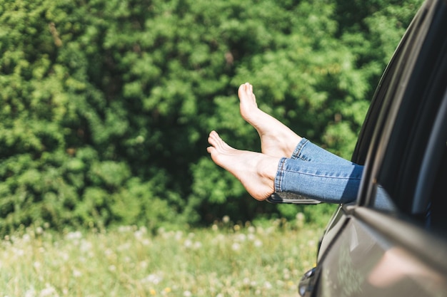 Jambes de femme mince pieds nus en jeans dans la fenêtre de la voiture sur le fond de la prairie d'été