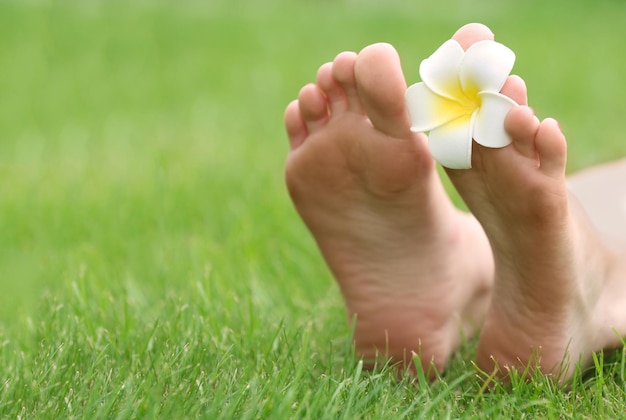 Jambes de femme avec plumeria sur l'herbe verte