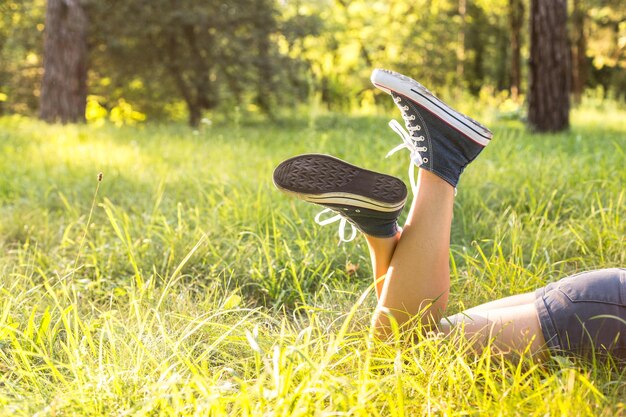 Jambes de femme portant des baskets jeans allongé sur une herbe dans une pelouse forestière le soir