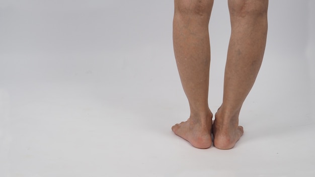 Jambes de femme senior ou plus âgée aux pieds nus debout sur fond blanc.