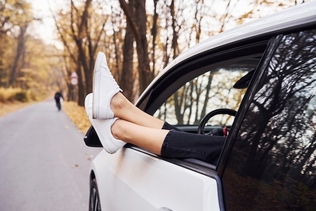 Les jambes de la femme sont hors de la fenêtre de la voiture. Nouvelle automobile moderne dans la forêt.