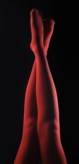 Jambes de femmes en collants rouges soulevées sur fond noir