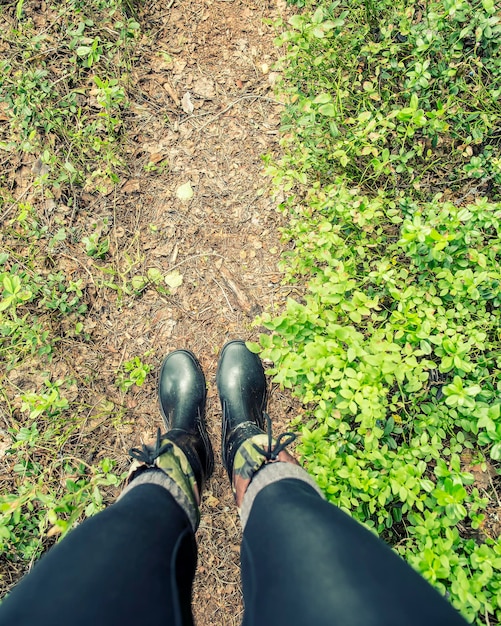 Les jambes des femmes dans des bottes en caoutchouc imperméables se tiennent sur un chemin forestier