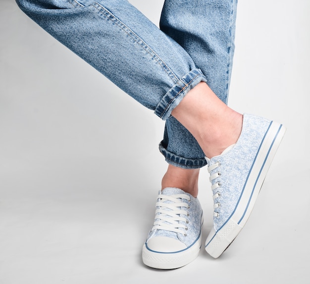 Les jambes des femmes en jeans courts et baskets se tiennent sur un blanc