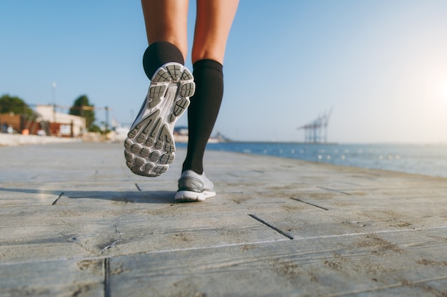 Les jambes de la fille en guêtres noires et baskets grises, qui court le matin à l'aube près de la mer