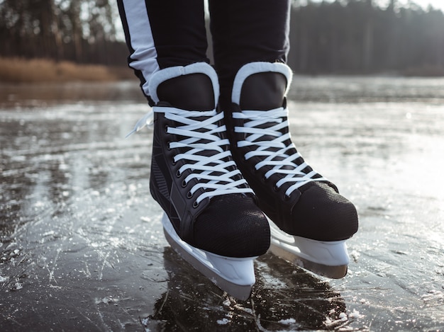 Jambes D'une Fille En Patins De Hockey Noir Sur La Glace D'un Lac En Gros Plan. Au Fond Une Forêt