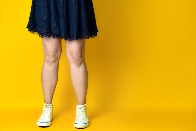 Jambes de fille vêtue d'une robe bleue sur fond jaune