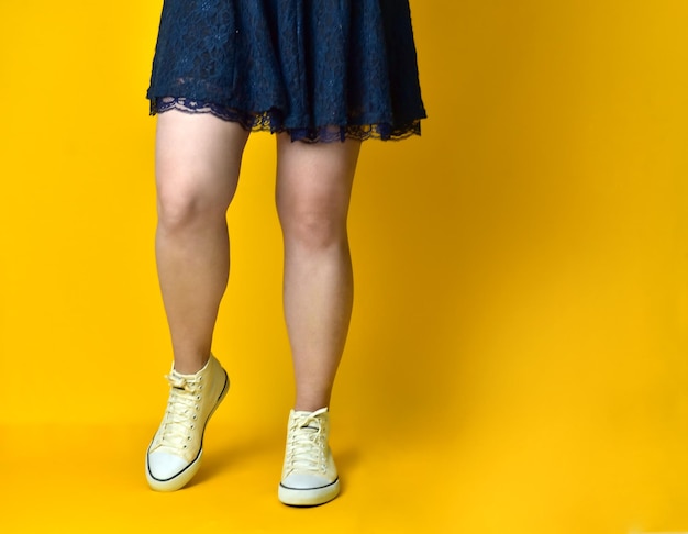 Jambes de fille vêtue d'une robe bleue sur fond jaune