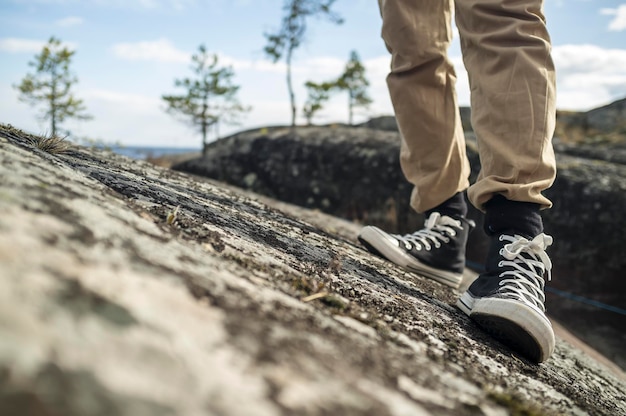 Jambes d'un homme en baskets noires sur les rochers sur fond de lac et de ciel bleu