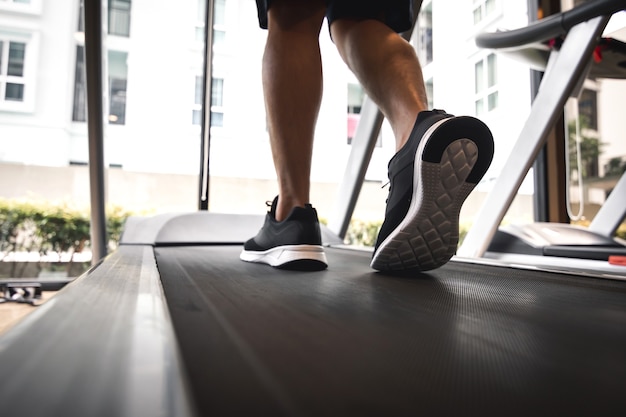 Jambes d'homme avec des chaussures de sport s'exécutant sur un tapis roulant dans une salle de fitness.