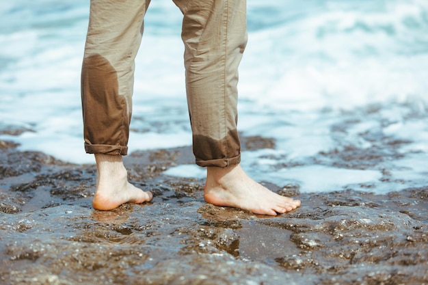 Jambes d'homme humides en pantalon marchant au bord de la plage rocheuse en profitant de l'eau. vacances d'été