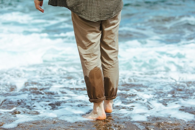 Jambes d'homme mouillé en pantalon marchant au bord de la mer plage rocheuse profitant de l'eau