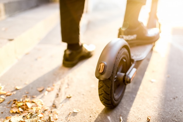 Jambes d'un homme en tenue élégante se tenir sur un scooter électrique dans la rue