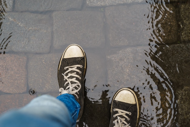 Les jambes des hommes en baskets marchant dans la flaque de pluie