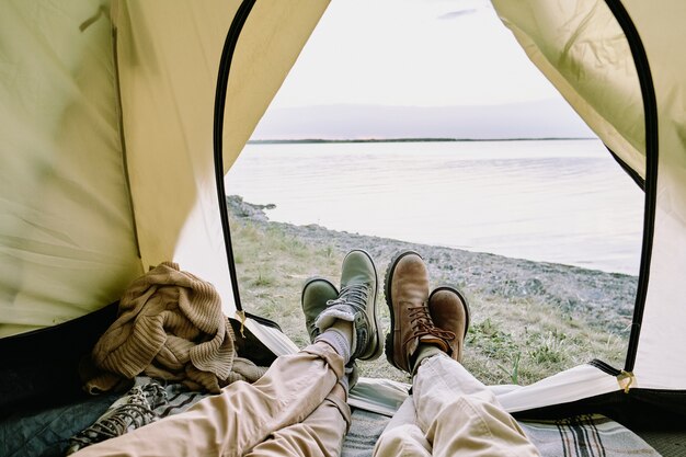 Jambes de jeune couple amoureux en tenue décontractée se trouvant à l'intérieur de la tente ouverte en face de la mer et se détendre lors d'une randonnée le week-end d'été