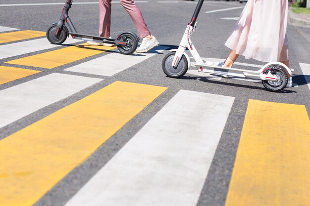 Jambes de jeune femme et jambes d'homme marchant avec des scooters sur la route transversale