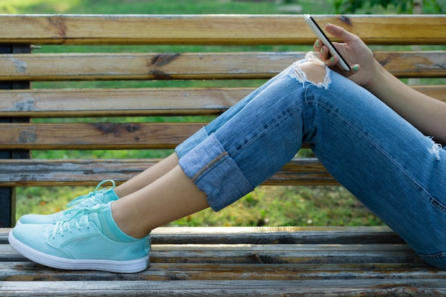 Jambes d&#39;une jeune femme en jeans sur un banc dans le parc