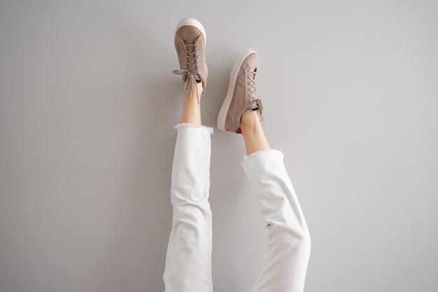 Jambes d'une jeune fille en jeans et baskets sur fond gris.