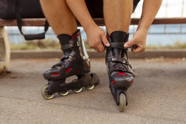 Les jambes d'un jeune homme mettant des patins à roulettes dans le parc