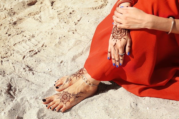 Jambes et mains femelles avec le tatouage de henné sur le fond de sable de plage